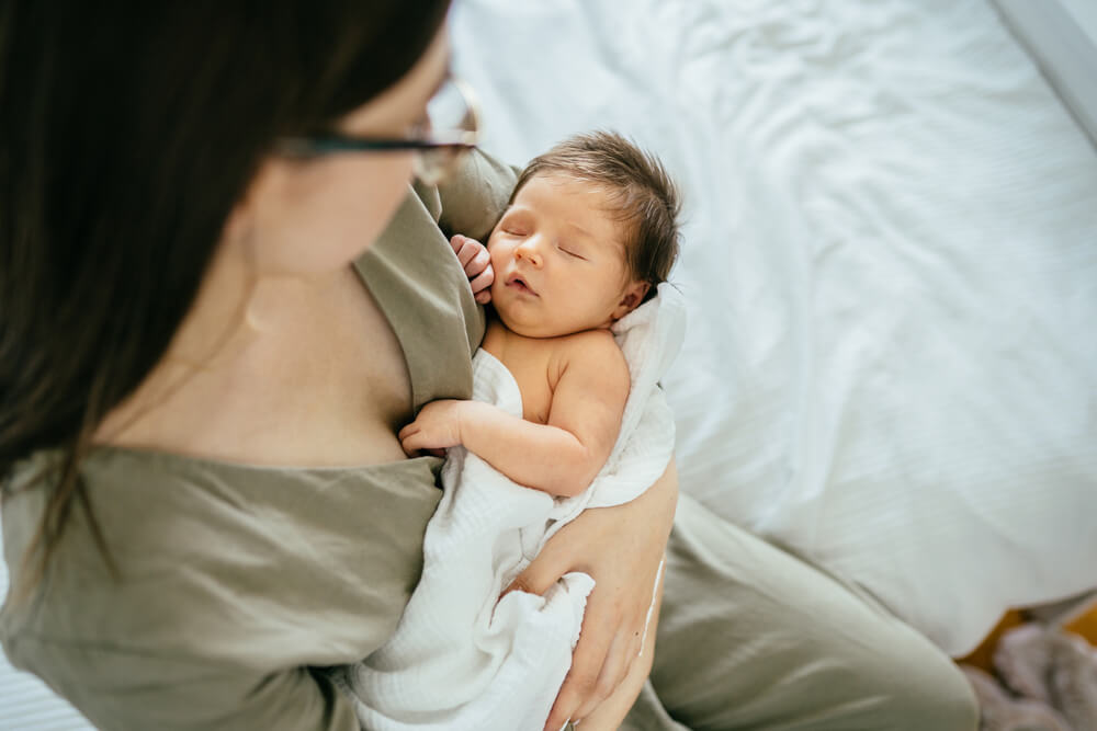 Caucasian Mother in Glasses Rocks the Child. Portrait of Sleeping Newborn in Mother’s Arms.