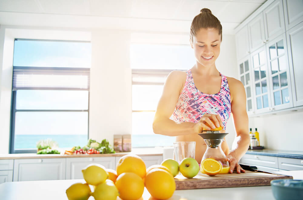 Fit Smiling Young Woman Preparing Healthy Fruit Juice From an Assortment of Fresh Fruit Using a Manual Juicer in Her Kitchen