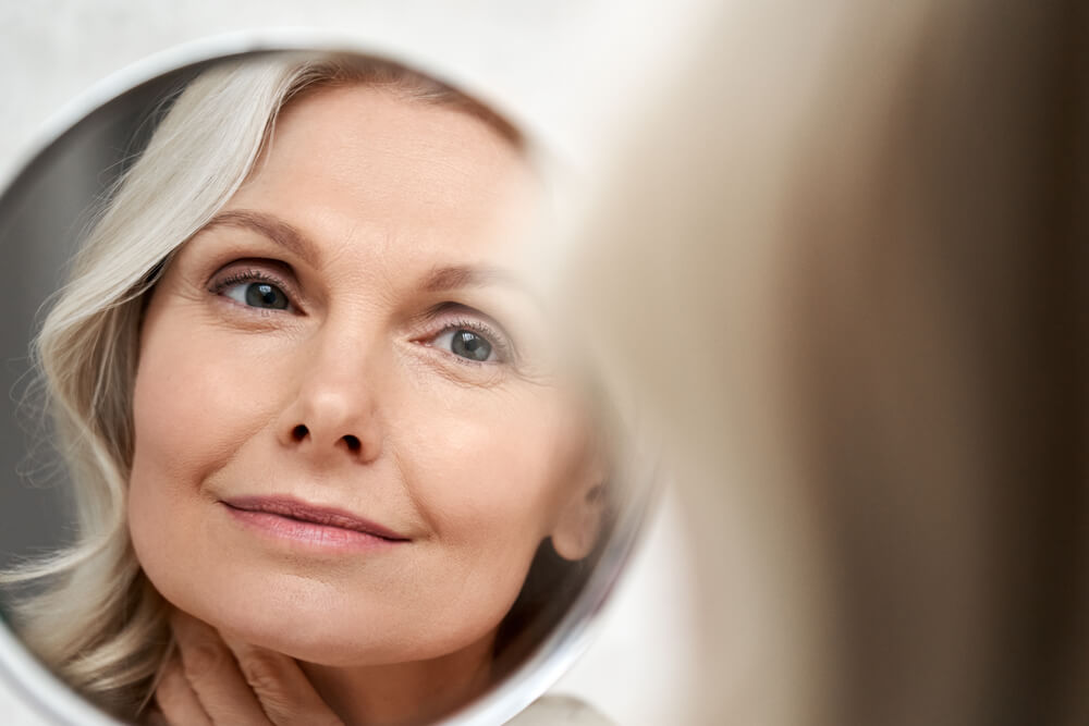 Happy 50S Middle Aged Woman Model Touching Face Skin Looking in Mirror Reflection