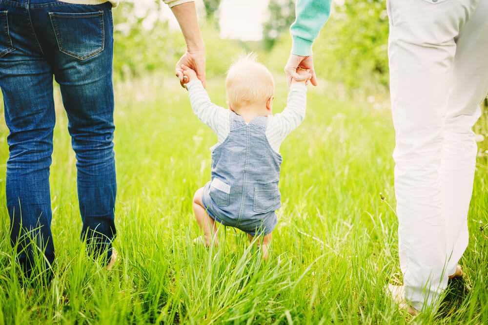 Portrait of a Happy Young Family Teaching Baby to Walk in the Park