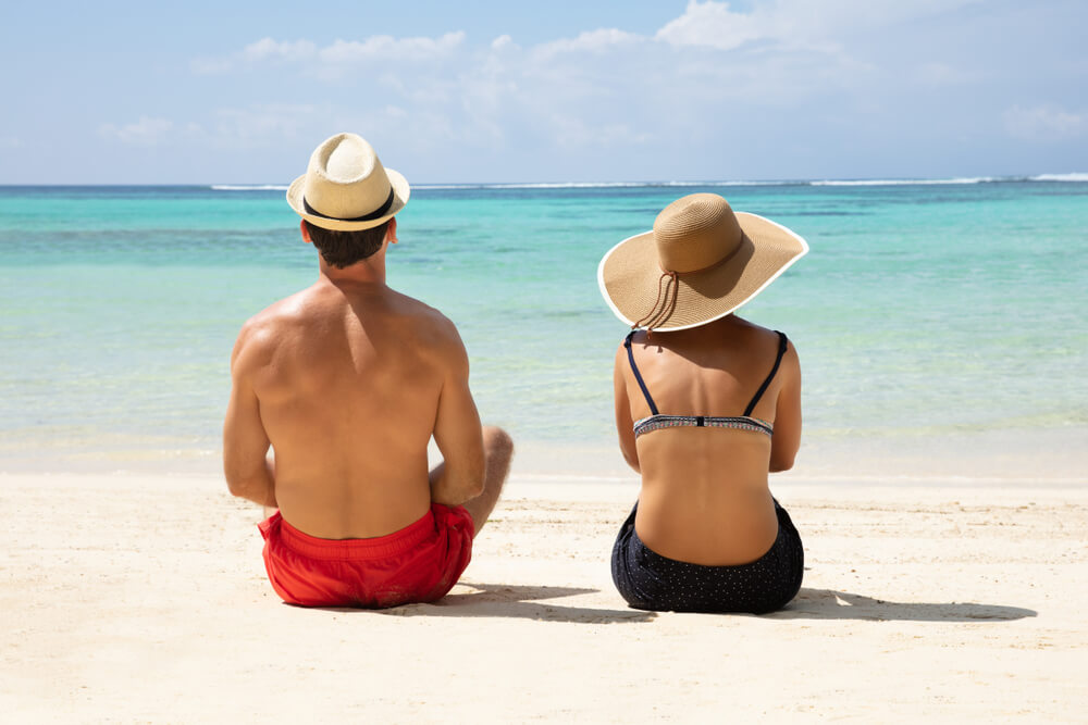Rear View of a Couple Wearing Hat Sitting on Sand Looking at Seascape