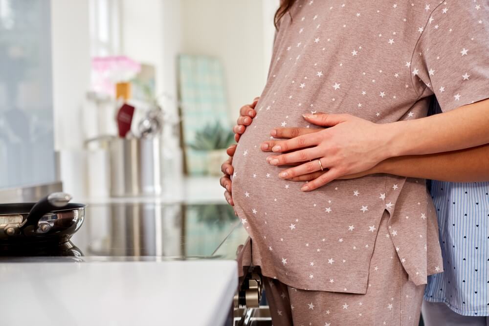 Close Up Of Same Sex Couple With Woman Holding Pregnant Partners Stomach At Home 