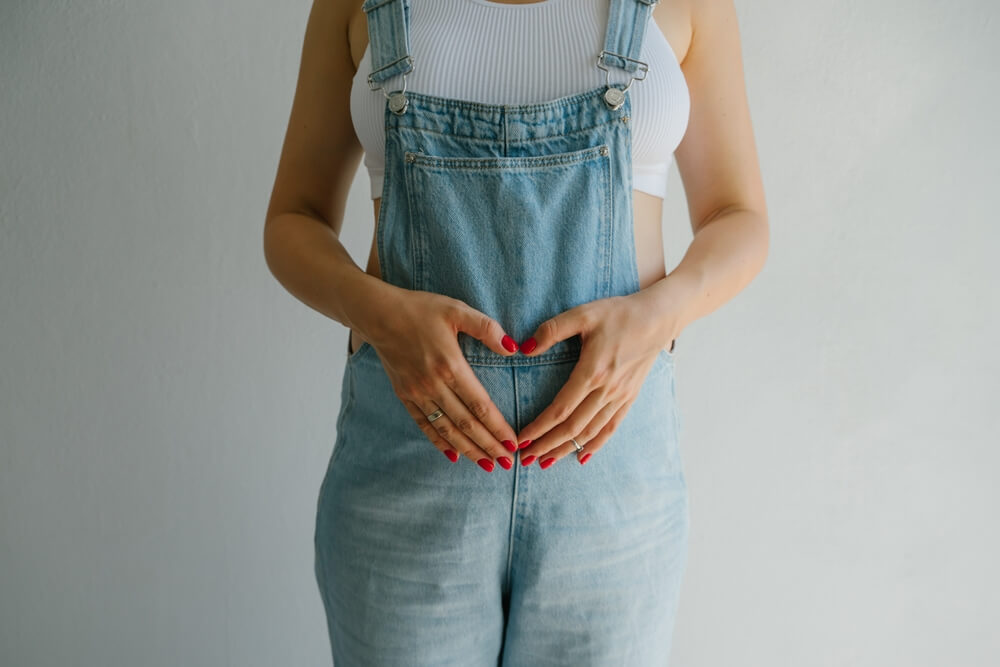Pregnant Girl in Denim Overalls. Hands on the Stomach Are Folded in the Shape of a Heart.