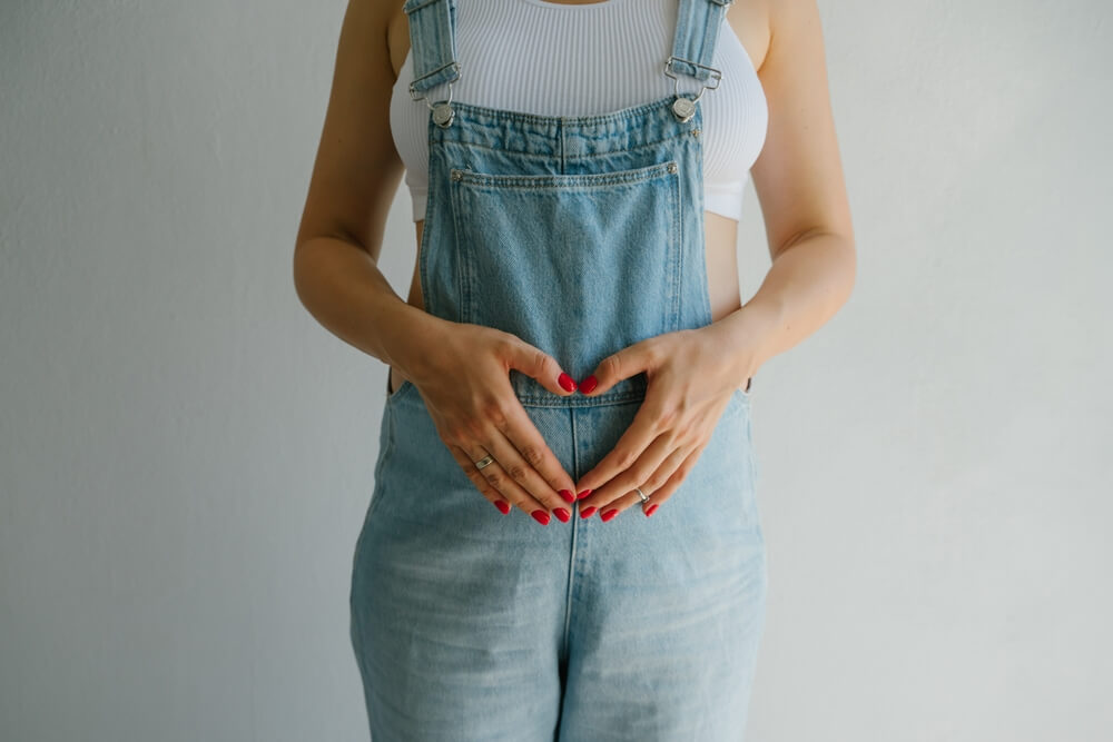 Pregnant Girl in Denim Overalls. Hands on the Stomach Are Folded in the Shape of a Heart.