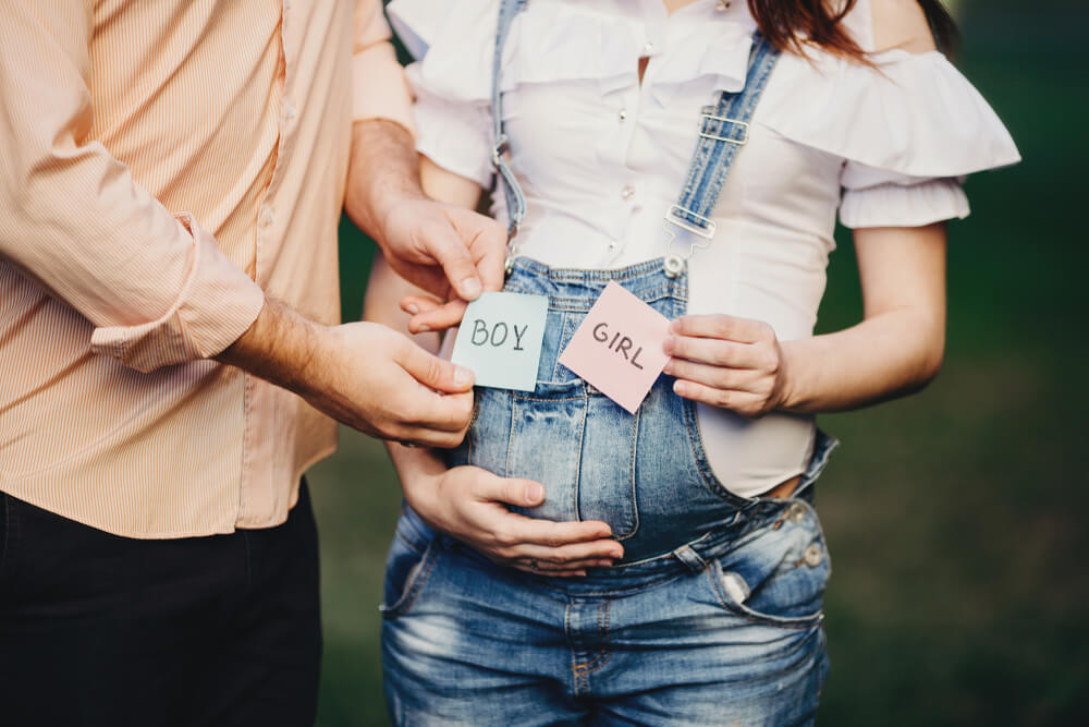 Male and Female Hands With Boy and Girl Cards Near Pregnant Woman Belly