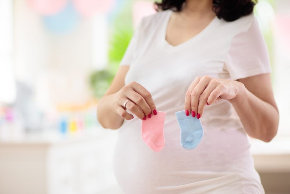 Pregnant woman holding gifts for newborn. Pink and blue decoration for baby girl or boy. 