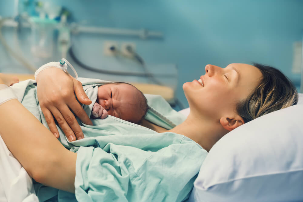 Mother and newborn. Child birth in maternity hospital. Young mom hugging her newborn baby after delivery. Woman giving birth. First moments of baby life after labor.