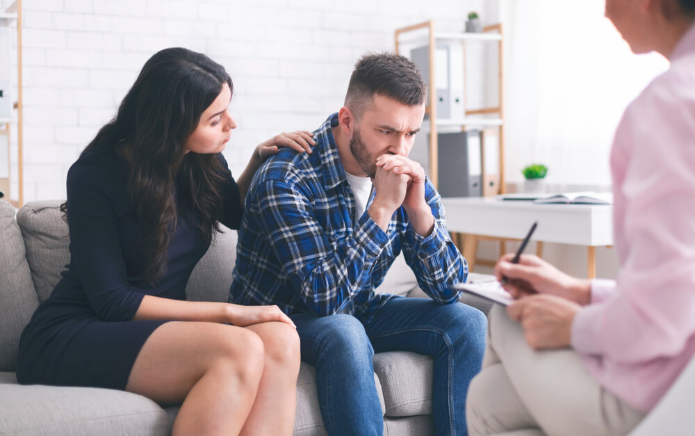 Loving Wife Supporting Her Depressed Husband During Psychotherapy Session With Counselor