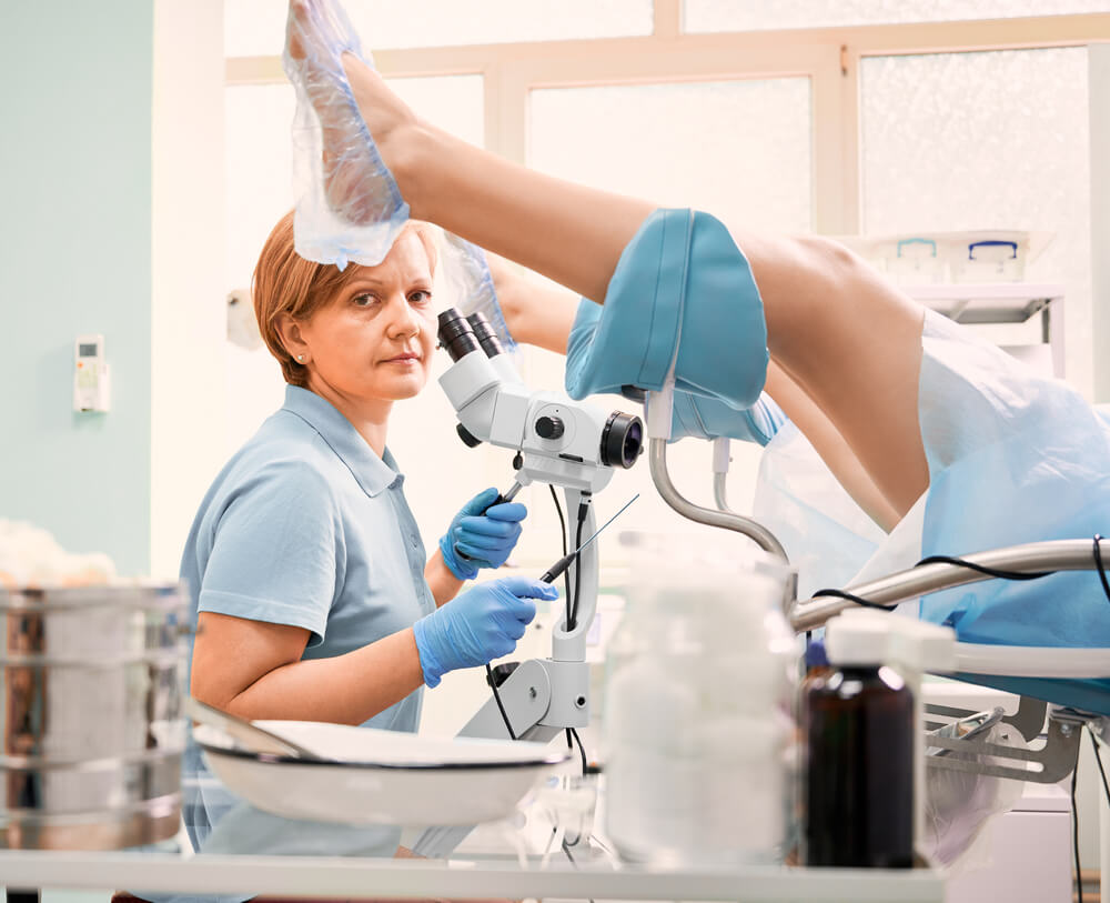 Female Patient in Shoe Covers Laying in Gynecological Chair While Doctor Doing Colposcopy Examination With Colposcope