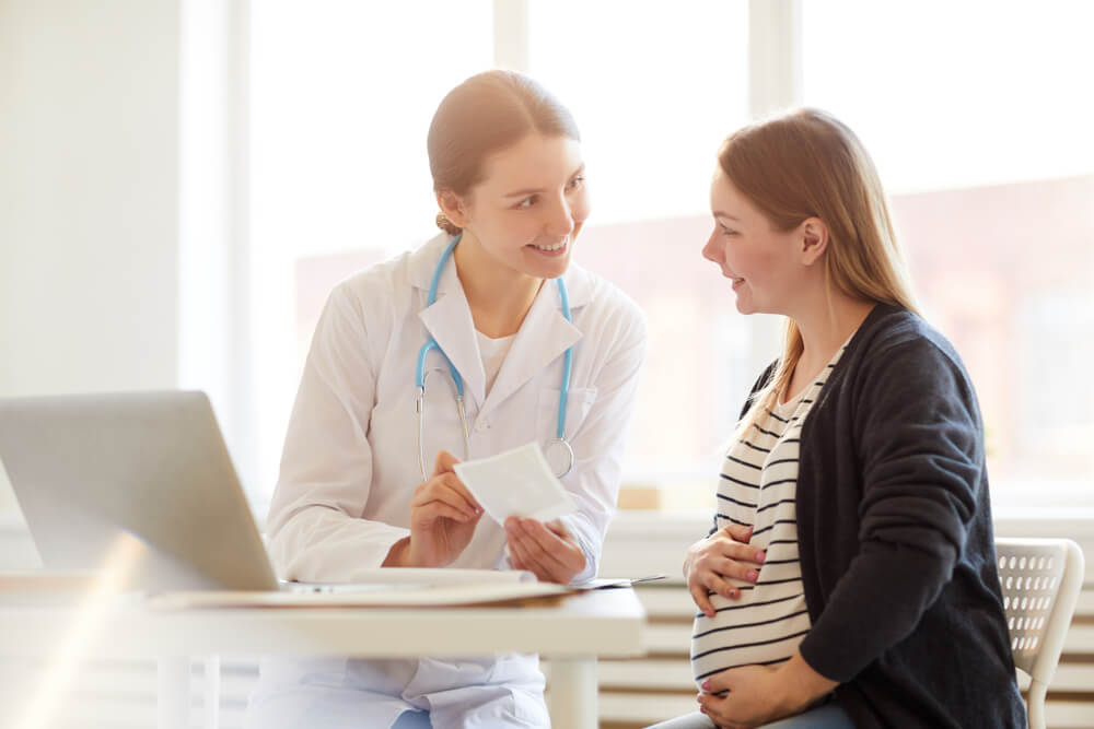 Portrait of Female Obstetrician Smiling at Pregnant Woman in Doctors Office