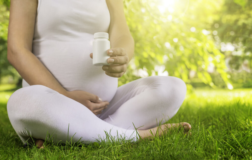 Pregnant Woman Holding Vitamin Pills in Her Hand and Relaxing in Nature on a Beautiful Sunny Day