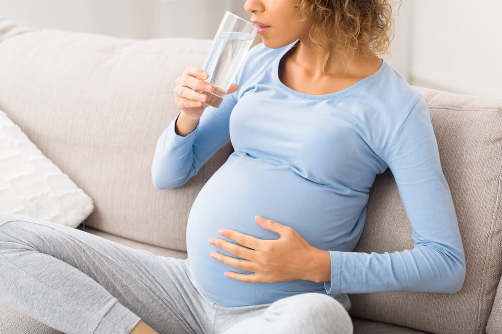 Pregnant Woman Drinking Water Sitting on Sofa, Resting at Home