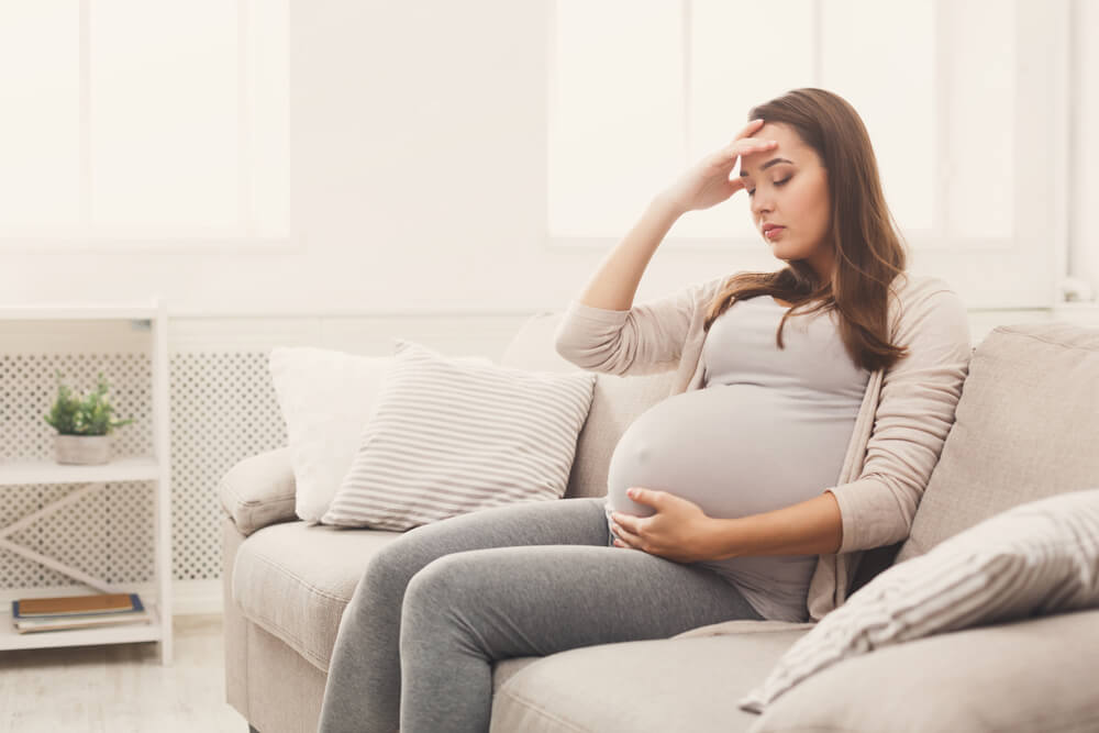 Young Pregnant Woman With Headache Sitting on Sofa.