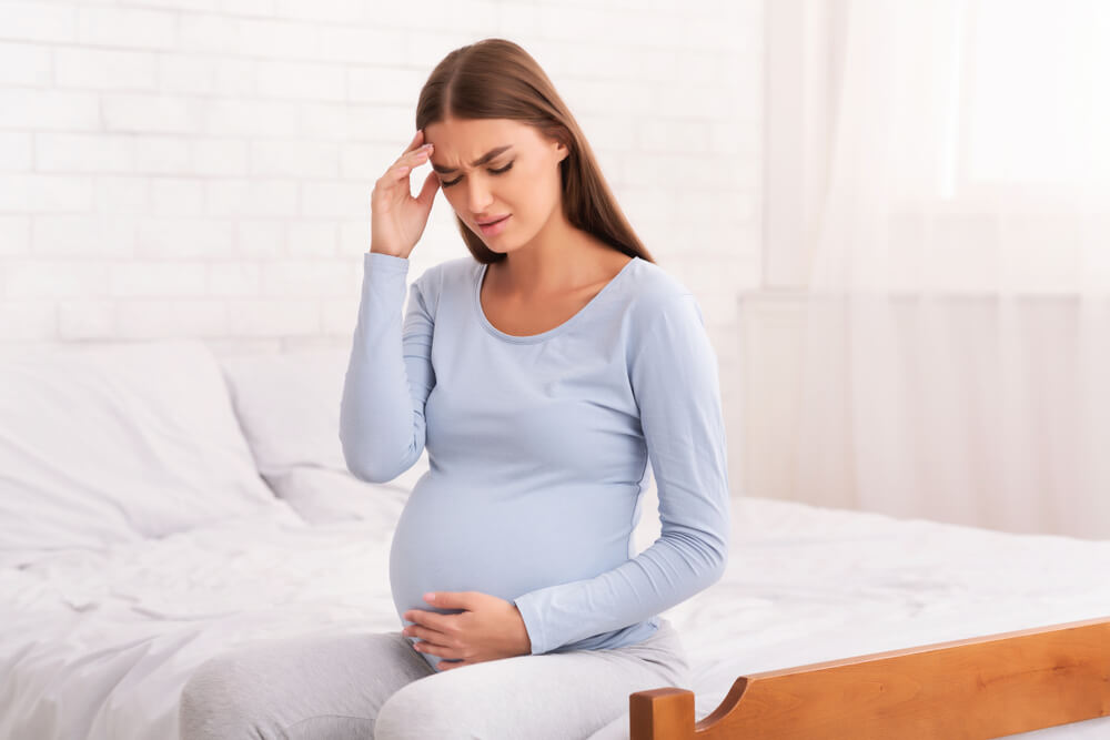 Beautiful pregnant woman in blue holds her head because she has problems with Dizziness During Pregnancy
