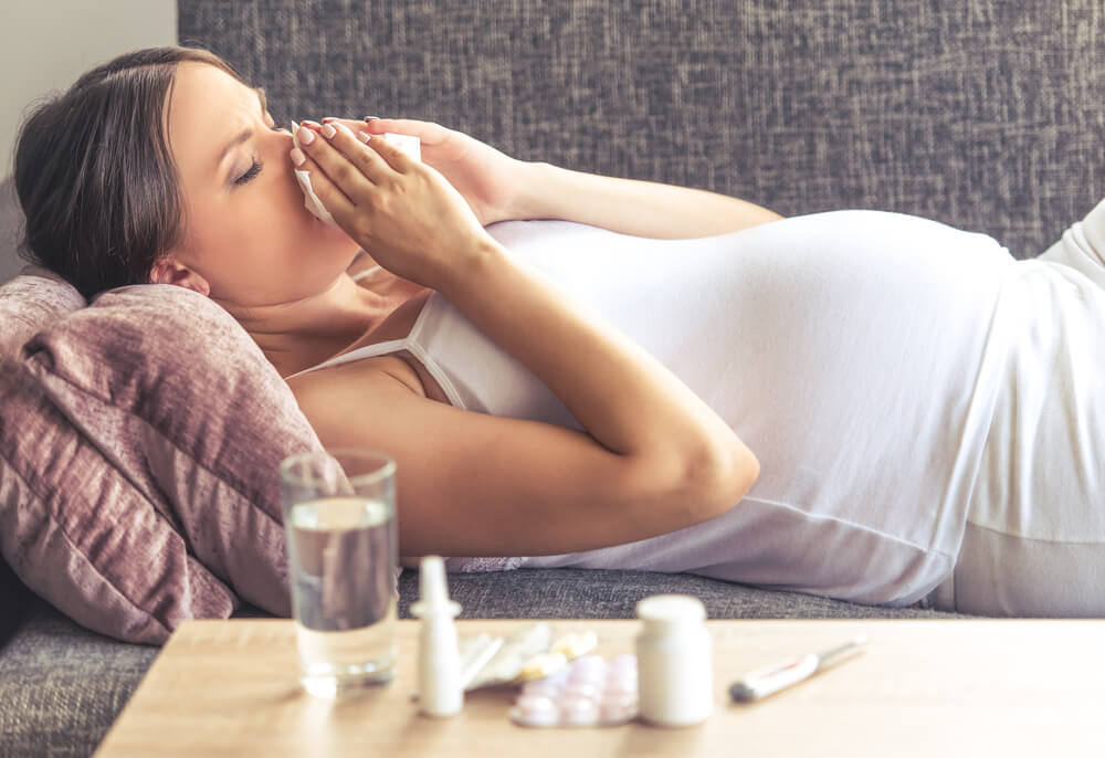 Side View of Beautiful Pregnant Woman Having Cold, Wiping Her Nose While Lying on Couch at Home.