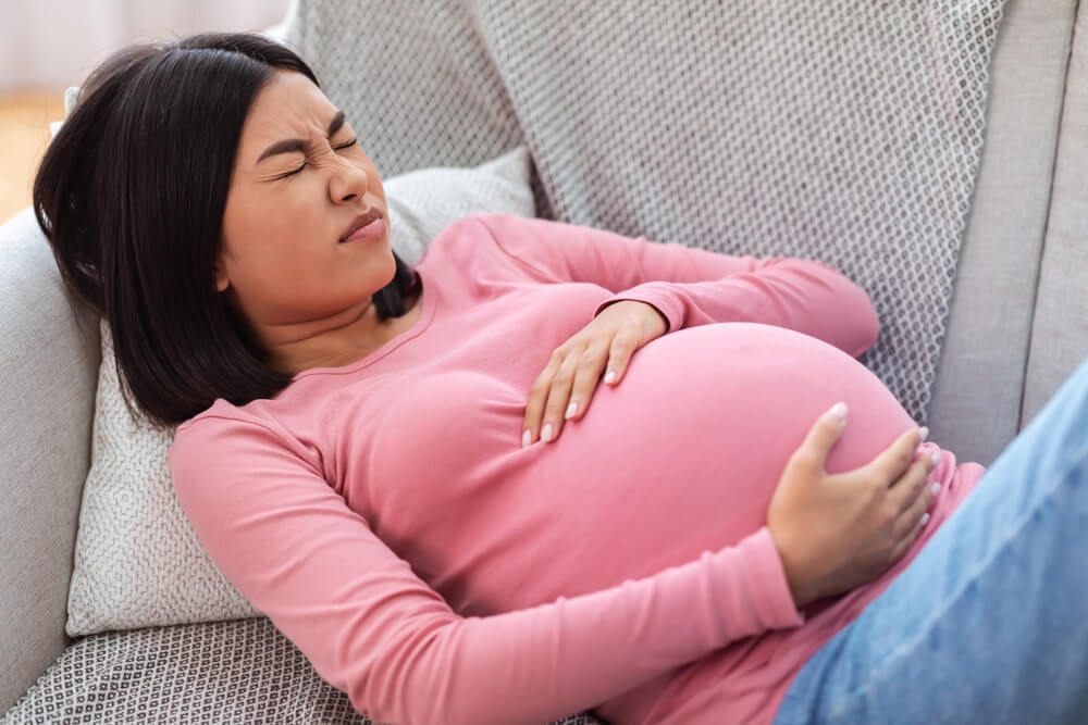 Pregnant Lady Suffering From Pain Touching Belly Having Painful Contractions Spasms Lying on Sofa at Home.
