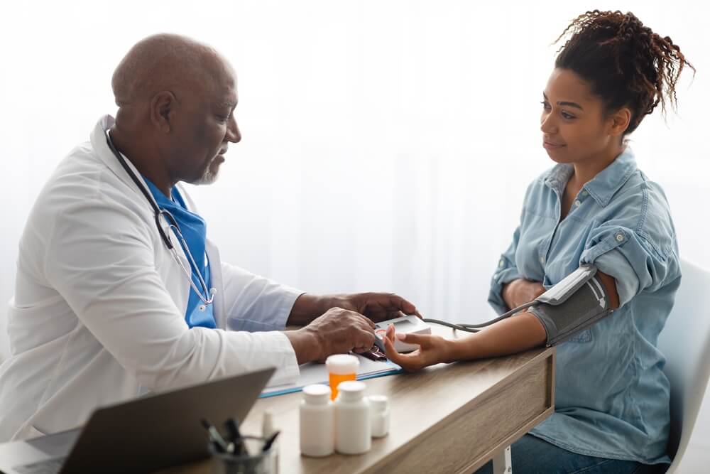 Mature Black Male Doctor Measuring Pregnant Patient’s Blood Pressure.