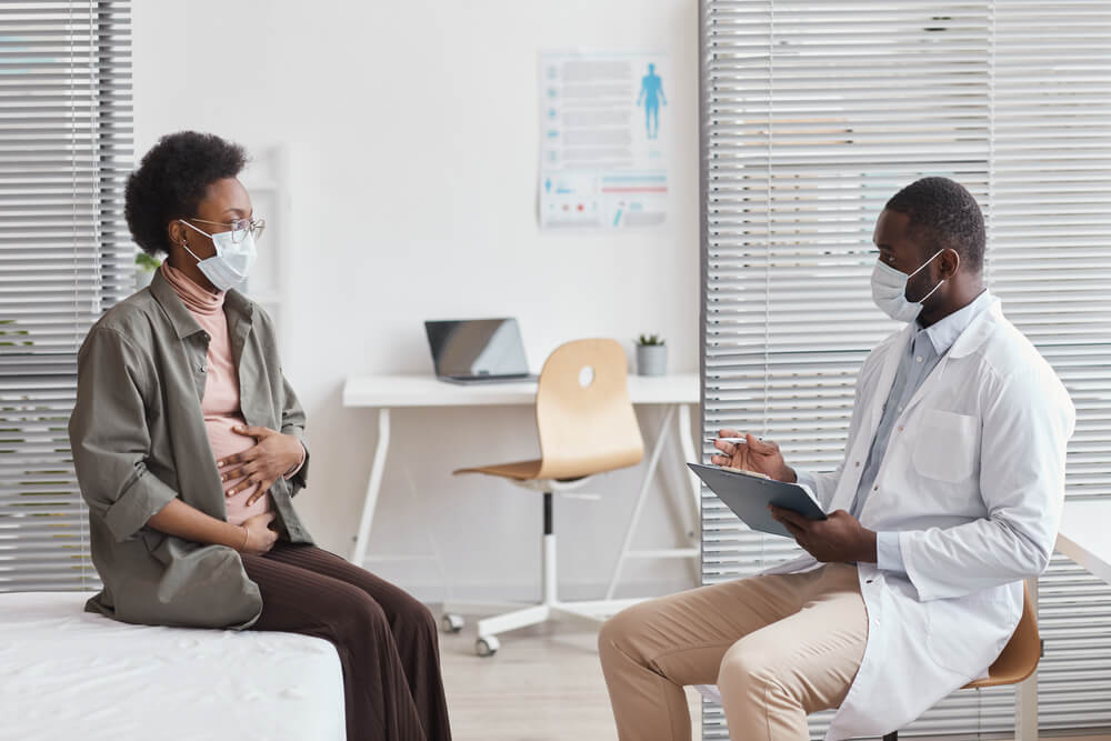 Pregnant Woman in Protective Mask Visiting the Doctor at Hospital and Talking To Him