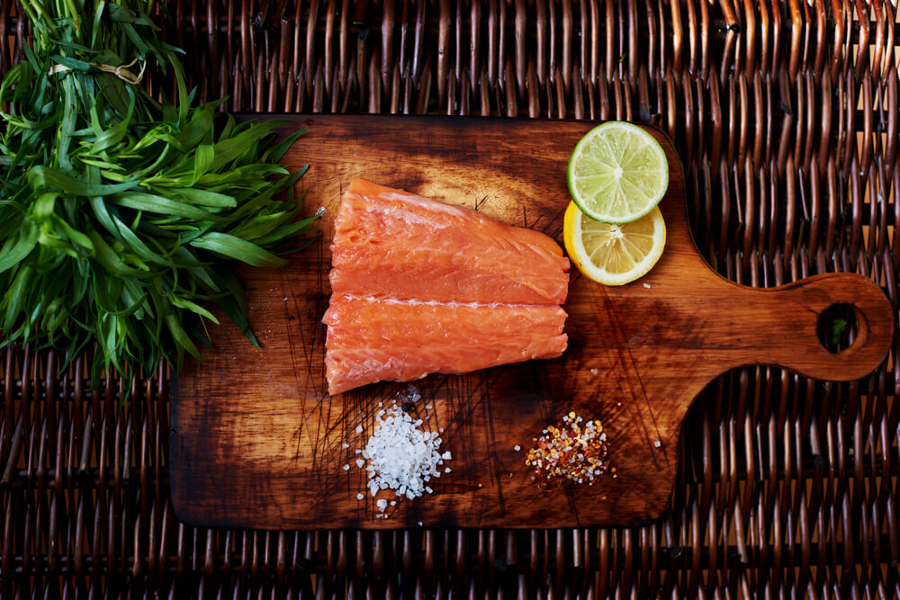 Small Piece of Salmon Is on the Board for Cutting Meat and Fish Is Scattered Next to the Salt and Pepper