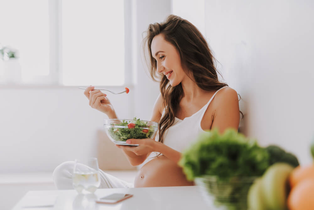 Profile Side View of Beautiful Mama Tasting Salad While Sitting on Chair in Bright Light Kitchen Inside Cozy Flat