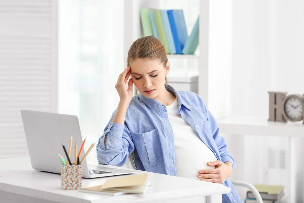 Pregnant Woman Suffering From Headaches While Sitting at Workplace in Light Room