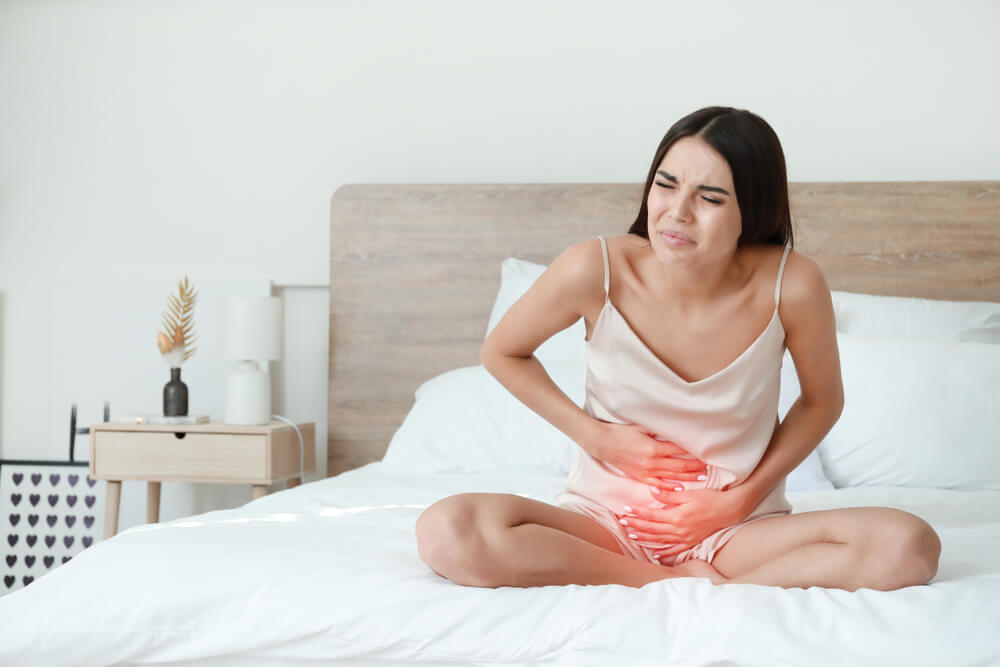 Young Woman Suffering From Menstrual Cramps in Bedroom