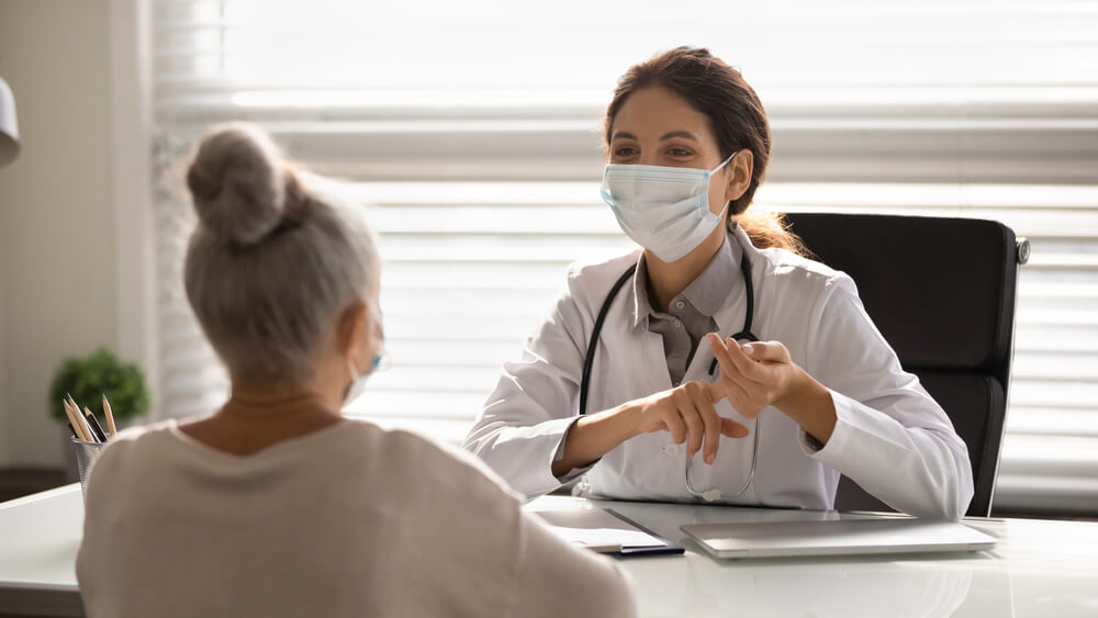 Female Doctor in Medical Facial Mask Have Consultation With Elderly Patient