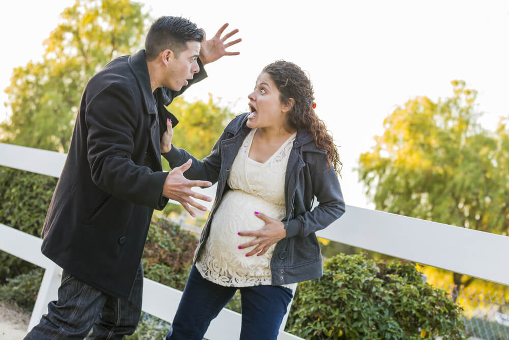 Stunned and Excited Pregnant Woman and Husband with Hand on Belly Outside.