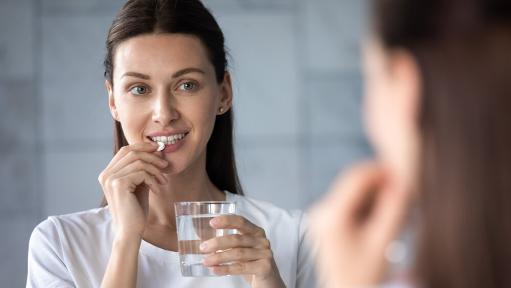 Young Healthy Woman Holding Pill Glass of Water Looking in Mirror, Adult Lady Take Daily Medicine Diet Vitamin Omega Supplements