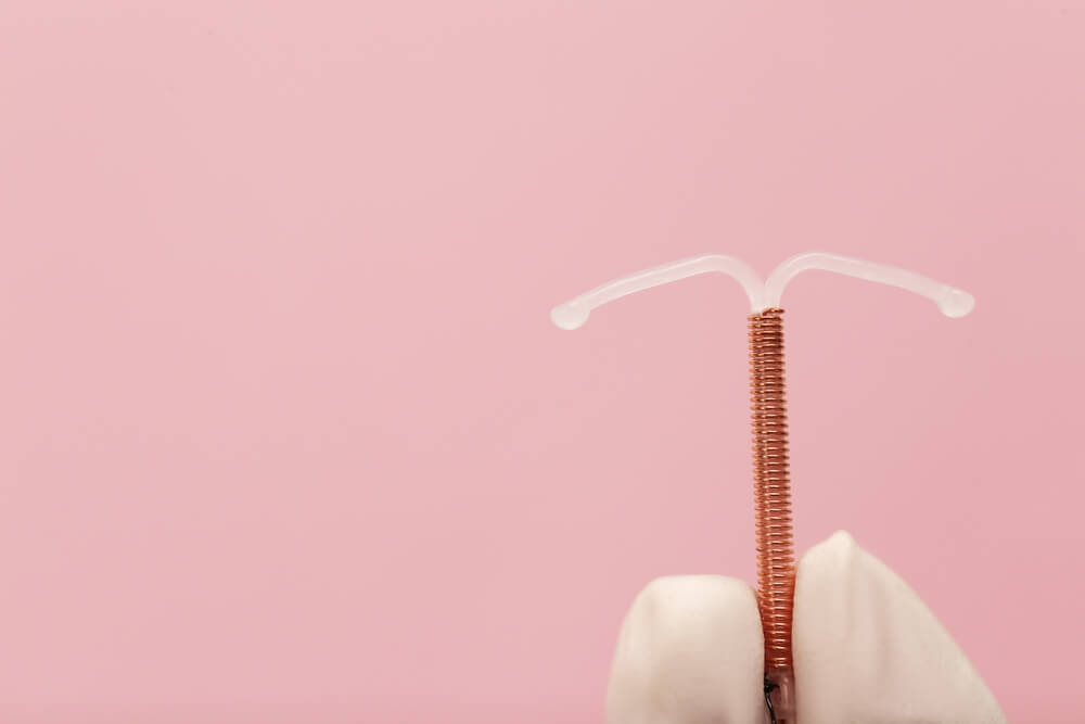 Doctor Holding T-Shaped Intrauterine Birth Control Device on Pink Background, Closeup
