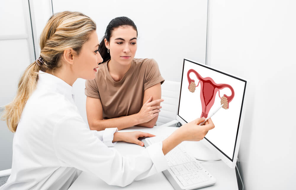 Gynecologist Consulting a Woman Patient and Pointing on Anatomical Illustration of a Uterus on a Monitor