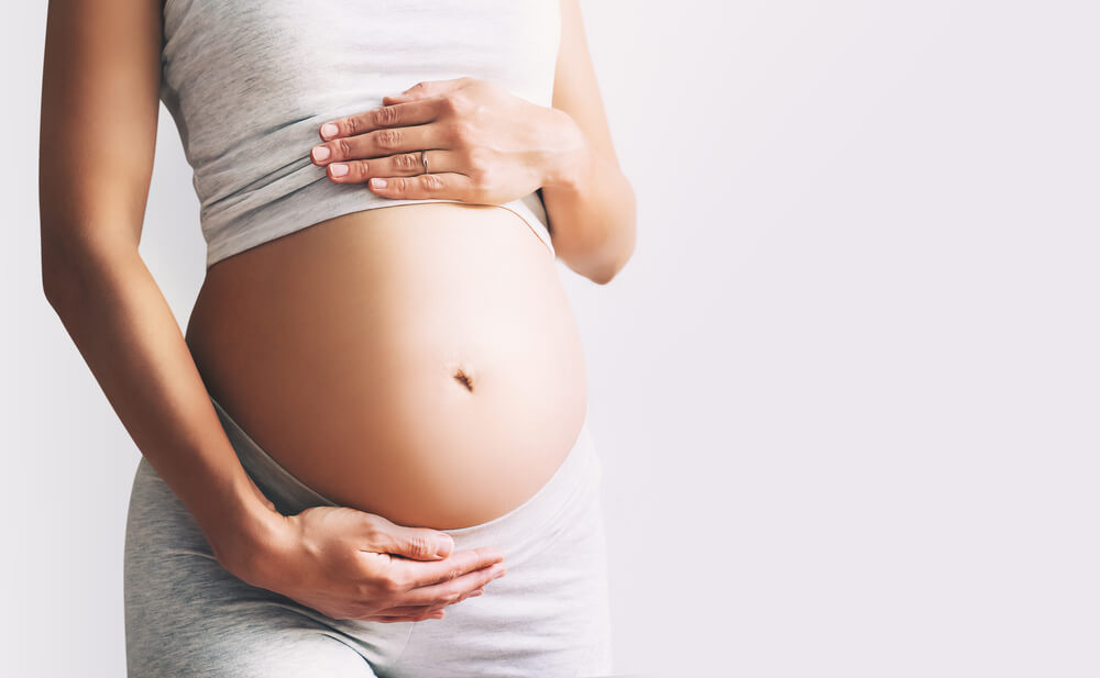 Pregnant Woman Holds Hands on Her Belly on White Background, Close-up