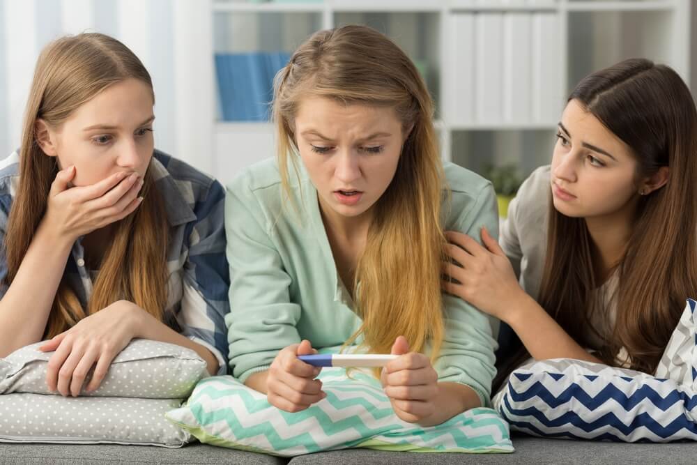 Terrified Teenage Girl Lying on Bed Holding a Pregnancy Test and Her Two Friends