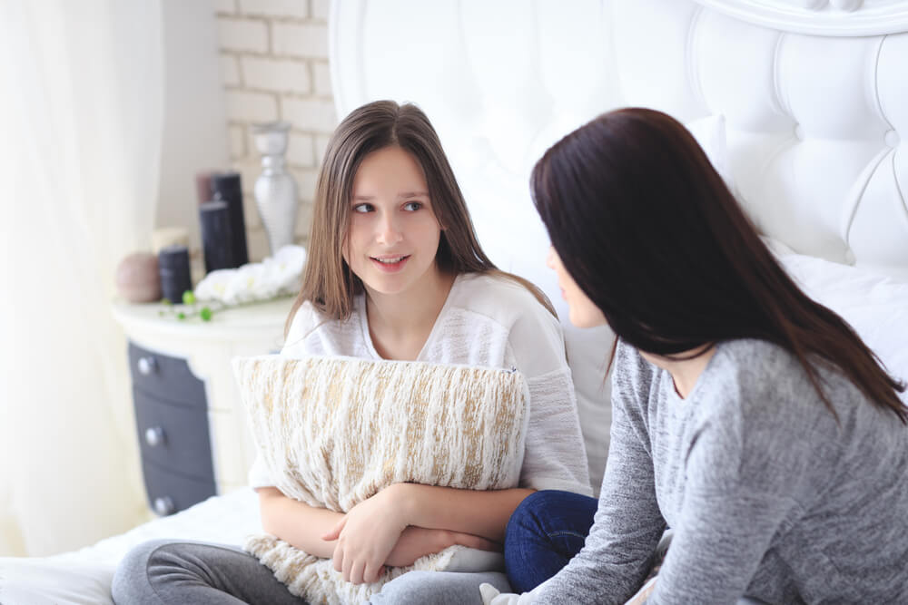 Beautiful Mother and Her Cute Teenage Daughter Talking Each Other, Sitting in Bedroom