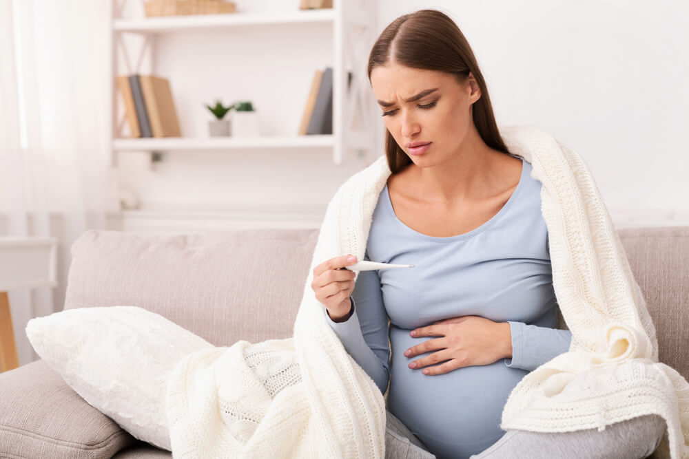 Fever During Pregnancy Pregnant Girl Holding Thermometer Measuring Temperature Feeling Bad Sitting On Sofa At Home Empty Space