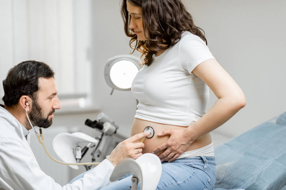 Male Doctor Listening to a Pregnant Woman's Belly With a Stethoscope During a Medical Examination in the Office