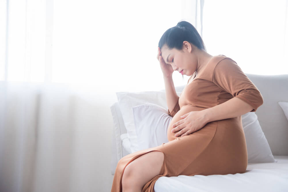 Middle Aged Pregnant Woman Sitting on Bed, Having Headache From Hypertension, High Blood Pressure.