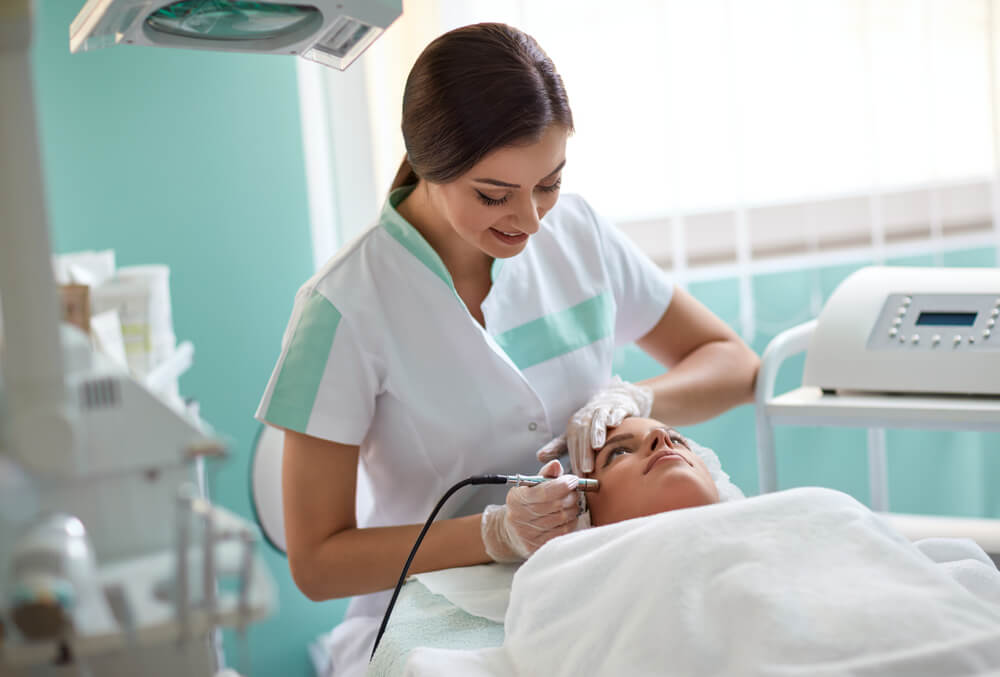 Professional Cosmetologist Treating Human Skin With Laser and Touching the Equipment to the Face