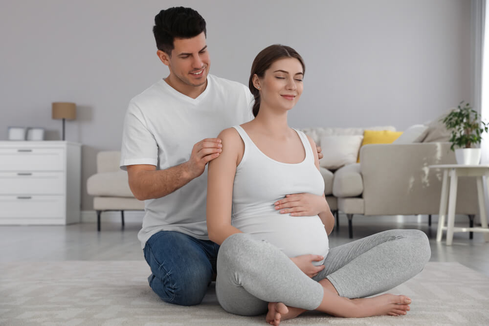 Husband Massaging His Pregnant Wife in Living Room.