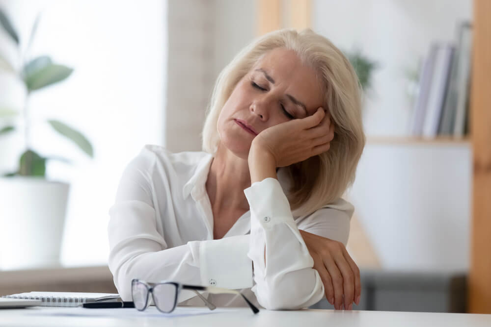 Exhausted Aged Woman Worker Sit at Office Desk Fall Asleep Distracted From Work
