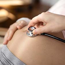 a doctor listening to a woman's pregnant belly with a stethoscope