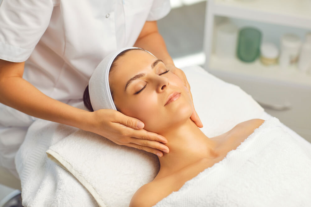 Hands of Cosmetologist Making Manual Relaxing Rejuvenating Facial Massage for Young Woman in Beauty Salon