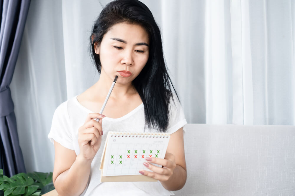 Asian Woman Having Problem With Amenorrhea, Irregular Periods Looking at Calendar and Counting Her Menstrual Cycles