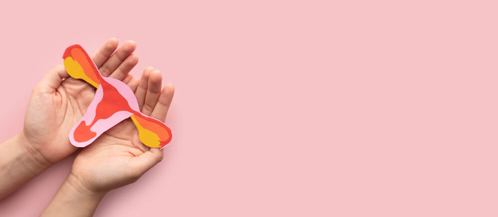 Woman Hand Holding Uterus Shape Made Frome Paper on Pink Background.