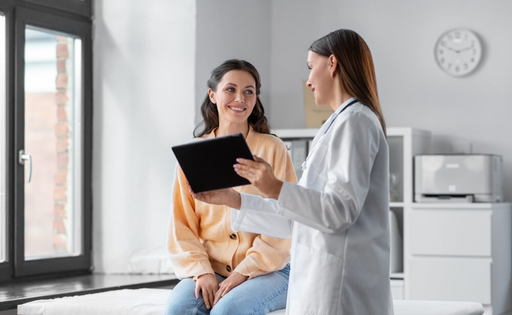 Medicine, Healthcare and People Concept - Female Doctor With Tablet PC Computer Talking To Smiling Woman Patient at Hospital