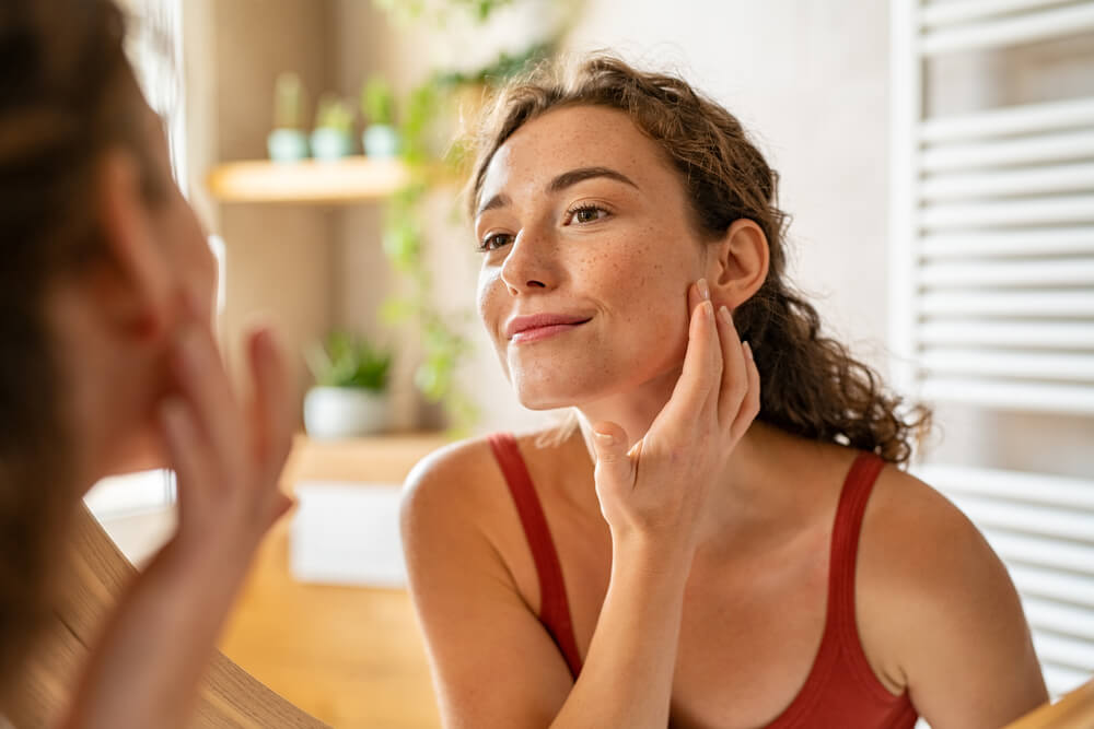 Happy smiling beautiful young woman applying moisturizer.