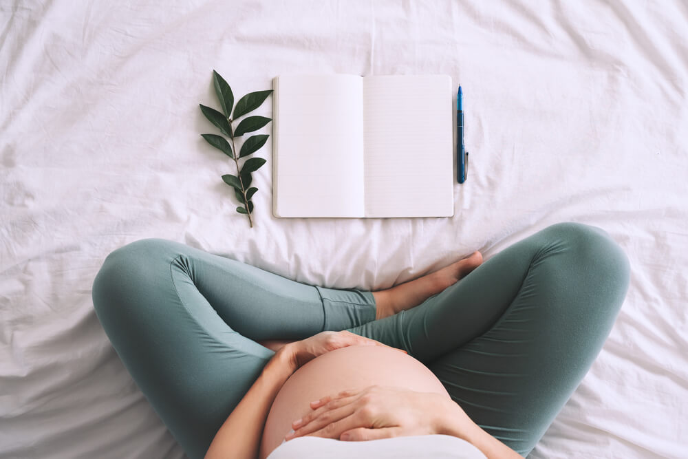 Pregnant Woman With Beautiful Belly Makes Notes or Check List in Paper Diary.