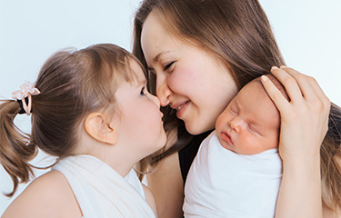 Mom holding her newborn baby and nuzzling her toddler, reflecting the tenderness of family moments.