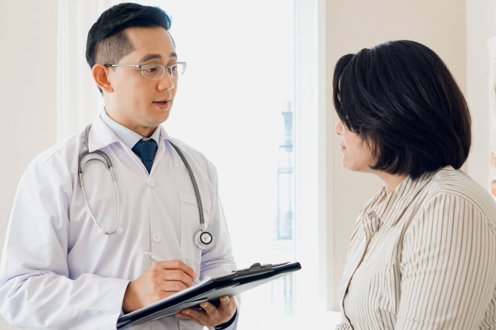 Asian Male Senior Doctor Explains Patient Treatment Information in Digital Tablet.