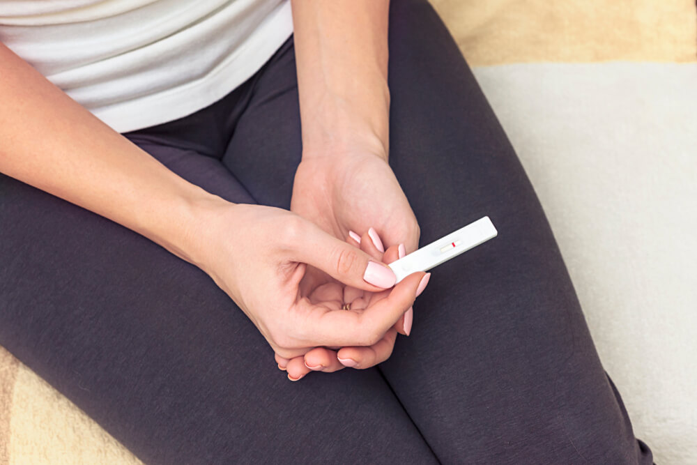 Female Hand With Pink Fingernails Holding Negative White Plastic Pregnancy Test.